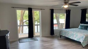 Ein Schlafzimmer mit einem Bett, einem Deckenventilator und großen Fenstern mit Vorhängen.