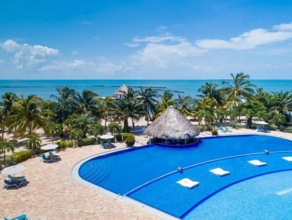 A resort with a large swimming pool, palm trees, and a beach view.