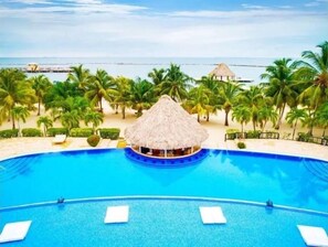 A swimming pool with a thatched-roof structure in the center, surrounded by palm trees and a beach view. - Luxury Waterfront Villa + FULL RESORT ACCESS! No sargassum! (Pla)