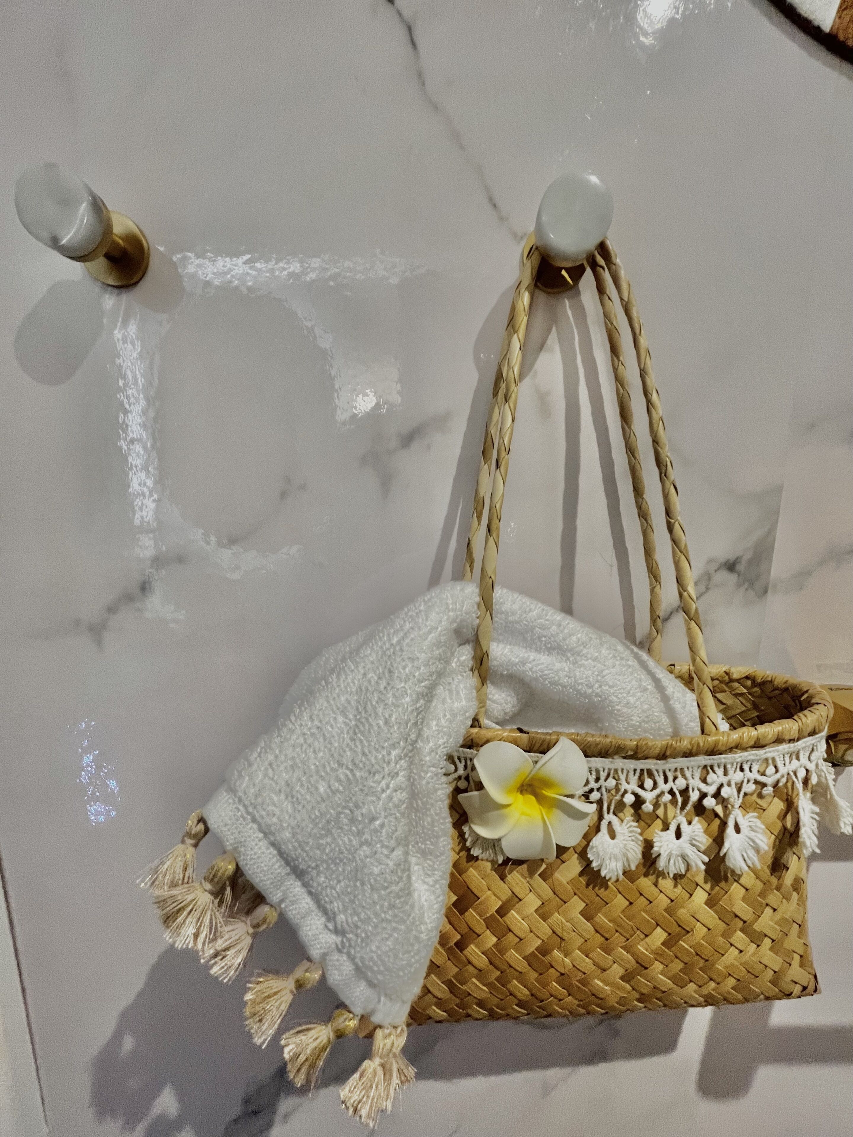 A woven basket with a white towel and decorative flowers, hanging on a marble wall.