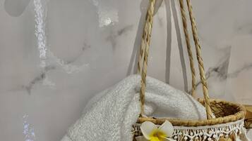A woven basket with a white towel and decorative flowers, hanging on a marble wall.