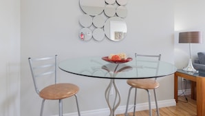 Un espace repas moderne avec une table en verre, deux chaises, un mur décoratif orné d’un miroir et une lampe.