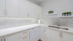 Une cuisine moderne avec des meubles blancs, un lave-vaisselle et un évier. On y trouve deux étagères ornées de plantes en pot.