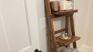 A wooden shelf unit with towels and toiletries against a white door. - The Resting Place Apt 1  Keep it simple at this peaceful & centrally located Apt (Marion)