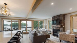 A spacious living area with a large dining table, sofas, and a fireplace. - New House on Big Sebago w/ Private beach & dock! (Casco)