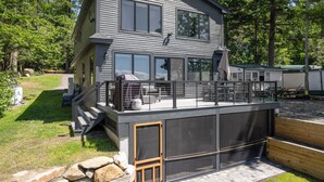 A two-story house with a balcony, large windows, and a garage. - New House on Big Sebago w/ Private beach & dock! (Casco)