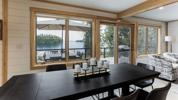 A dining area with a large table, four candles, and a view of a lake and outdoor seating. - New House on Big Sebago w/ Private beach & dock! (Casco)