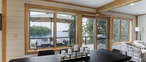 A dining area with a large table, four candles, and a view of a lake and outdoor seating.