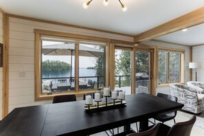 A dining area with a large table, four candles, and a view of a lake and outdoor seating.