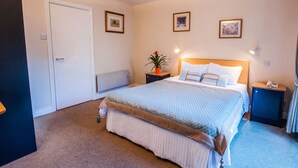 Une chambre d’hôtel avec un lit, des tables de chevet, une petite table, une plante en pot et des tableaux encadrés au mur.
