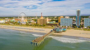 A coastal cityscape with a pier extending into the water, a large Ferris wheel, and several multi-story buildings.