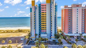 A multi-story hotel with balconies, a parking area, and a view of the beach.