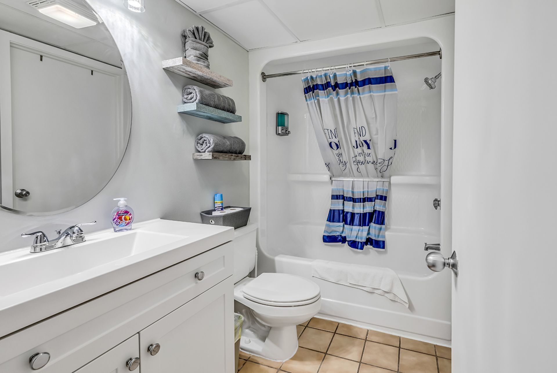 Une salle de bain avec un lavabo blanc, des toilettes, une baignoire et un rideau de douche à rayures bleues.