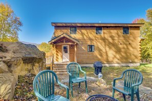 Une cabane en rondins avec un porche, deux chaises en plastique vertes et un barbecue.