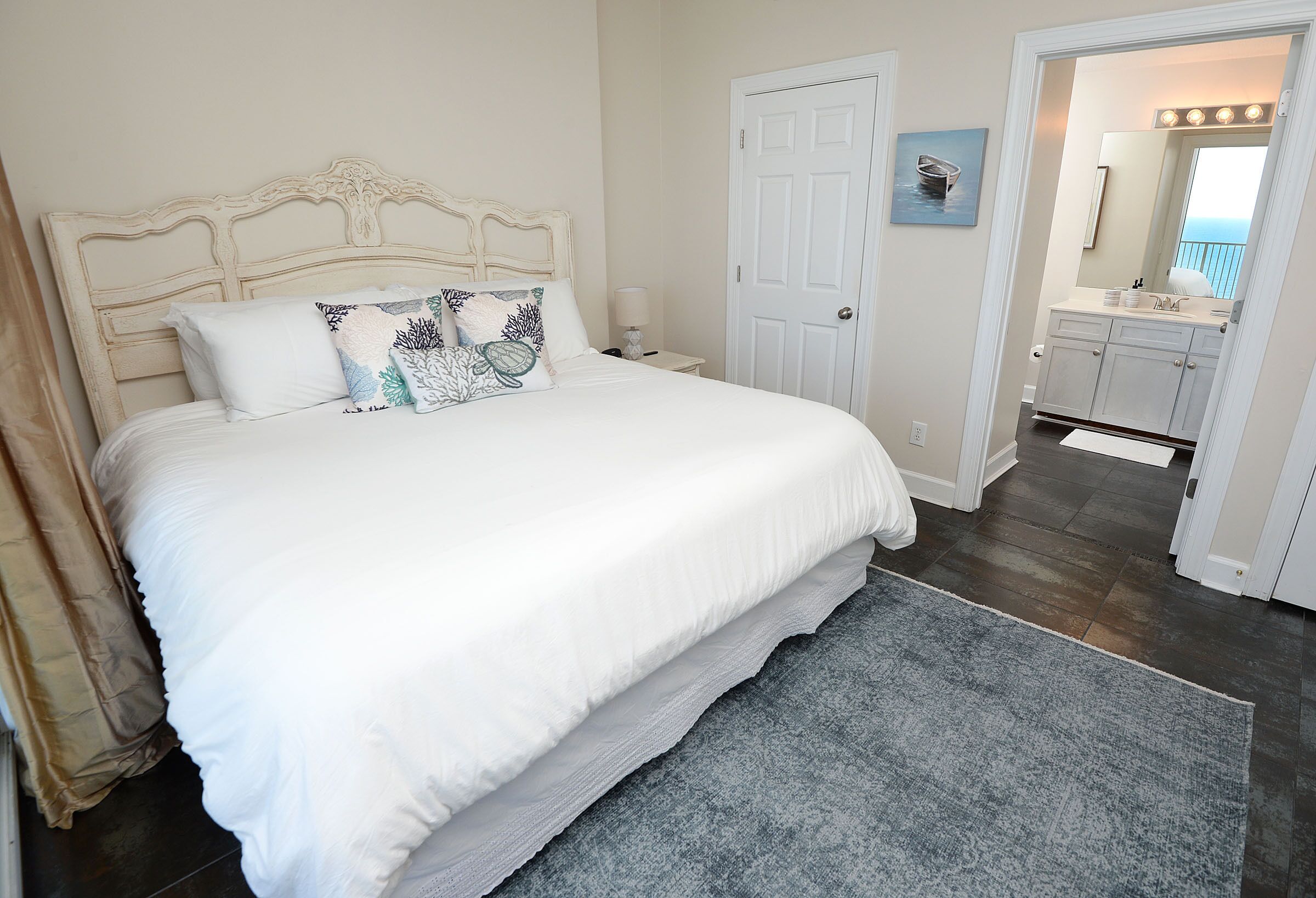 A bedroom with a large bed, a nightstand, a door, and a bathroom visible through an open door.