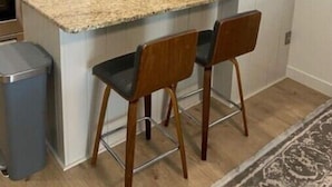 Une cuisine moderne avec des meubles blancs, un plan de travail en granit et deux tabourets de bar.