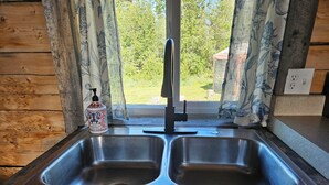 A kitchen with a double stainless steel sink, wooden cabinets, and a window with curtains.