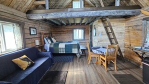 A rustic cabin interior with a bed, a sofa, a dining table, and a kitchen area.