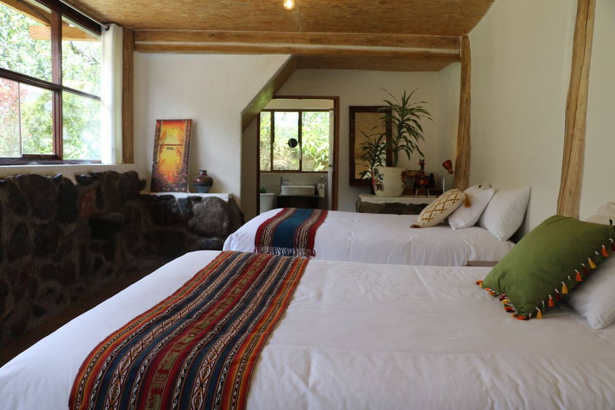 A bedroom with two beds, a stone wall, a window, and a painting.