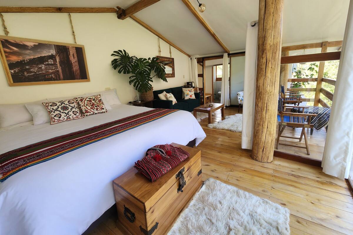 A spacious bedroom with a large bed, wooden furniture, a potted plant, and a view of the outdoors.