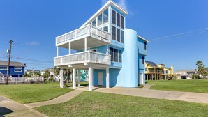 Een gebouw met twee verdiepingen, een balkon op de bovenste verdieping, een overdekte veranda beneden en een helderblauwe lucht erachter.