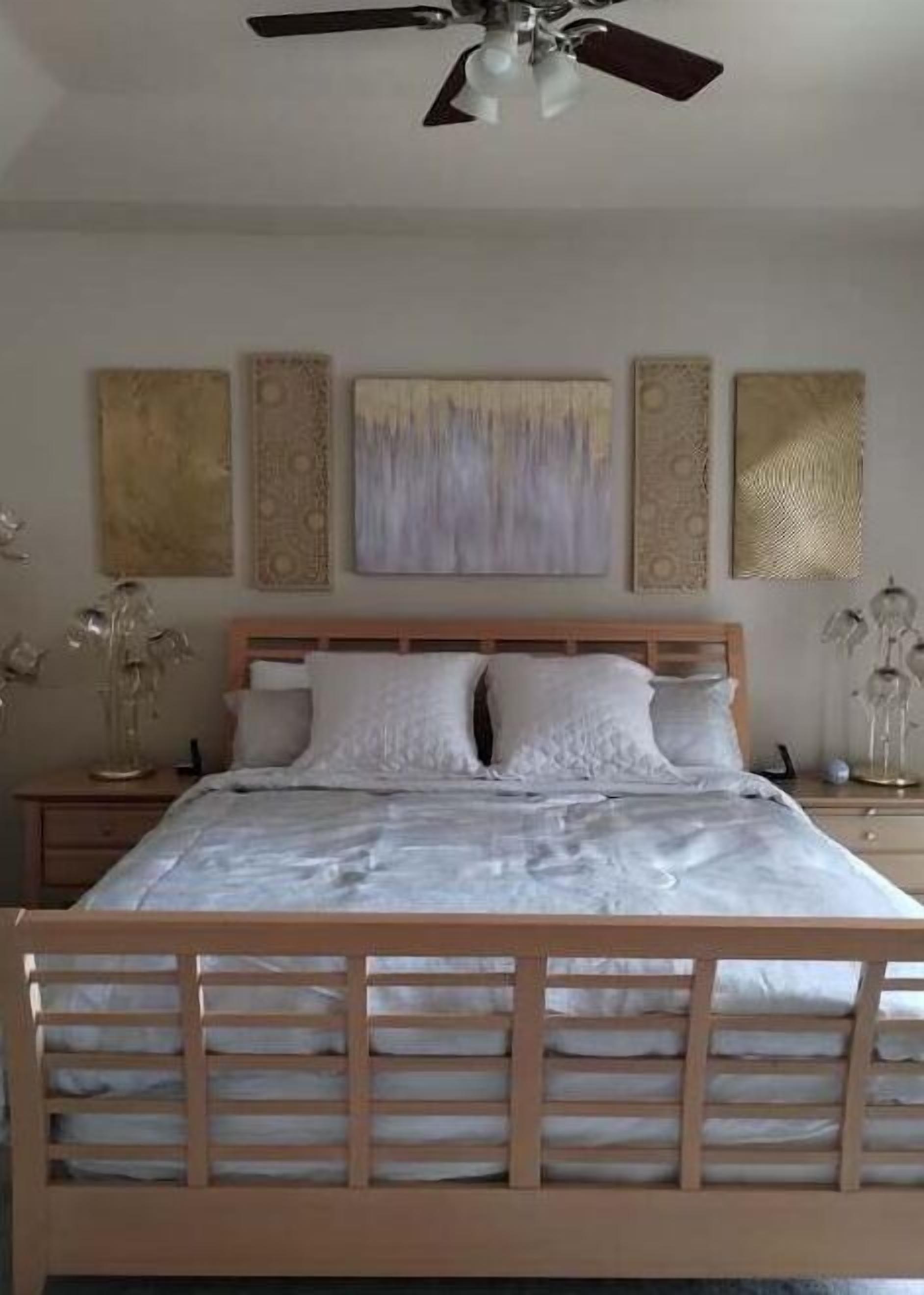 Une chambre à coucher avec un lit en bois, un ventilateur de plafond et des œuvres d’art murales.