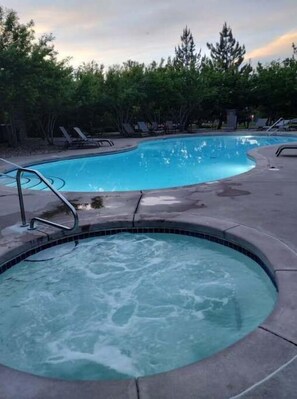 A swimming pool with a hot tub in the foreground, surrounded by lounge chairs and trees. - Westbury Townhome with community pool (Northglenn)