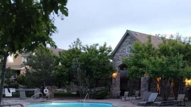 A swimming pool with lounge chairs and a stone building in the background. - Westbury Townhome with community pool (Northglenn)