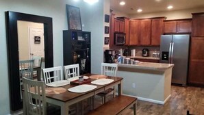 A dining area with a wooden table and chairs, a kitchen with wooden cabinets and appliances, and a small island with a sink. - Westbury Townhome with community pool (Northglenn)