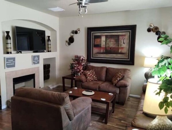 A living room with a sofa, armchair, coffee table, fireplace, television, and a framed artwork on the wall. - Westbury Townhome with community pool (Northglenn)