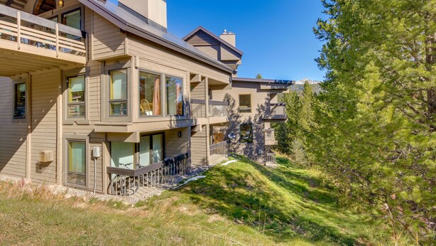 A multi-story house with a balcony, large windows, and a view of trees and mountains. - Cozy Condo w/ Balcony - Near Big Sky Resort! (Big Sky)