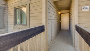 A narrow wooden corridor with a metal railing, a window with blinds, and a door at the end. - Cozy Condo w/ Balcony - Near Big Sky Resort! (Big Sky)