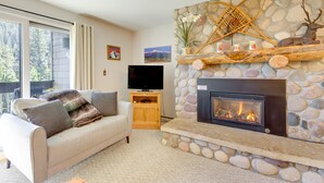 A cozy living room with a stone fireplace, a flat-screen TV, and a comfortable sofa. - Cozy Condo w/ Balcony - Near Big Sky Resort! (Big Sky)
