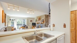 A modern kitchen with a large sink, a dishwasher, and a stone wall decoration. - Cozy Condo w/ Balcony - Near Big Sky Resort! (Big Sky)
