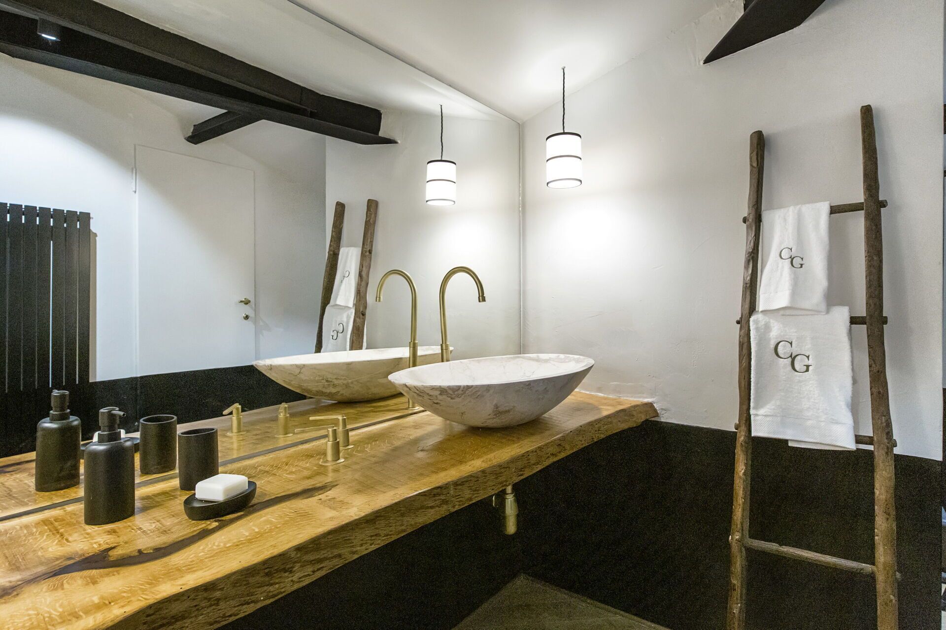 Ein modernes Badezimmer mit zwei großen Marmorwaschbecken, einem Holzwaschtisch und einer Wandleiter.