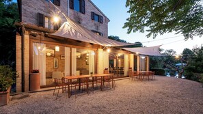 A modern outdoor dining area with a covered patio, wooden furniture, and a stone wall backdrop.