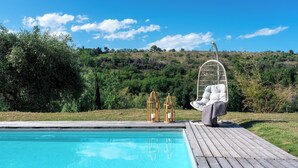 A wooden deck with a pool, a wicker chair, and two lanterns. - I Lauri 12, Emma Villas (Massignano)