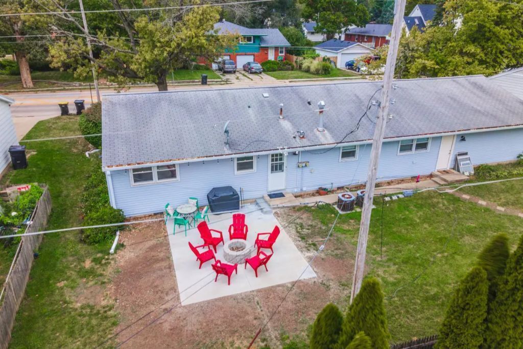 Une maison d’habitation à l’extérieur bleu, dotée d’un patio couvert avec des chaises rouges et d’un foyer extérieur.