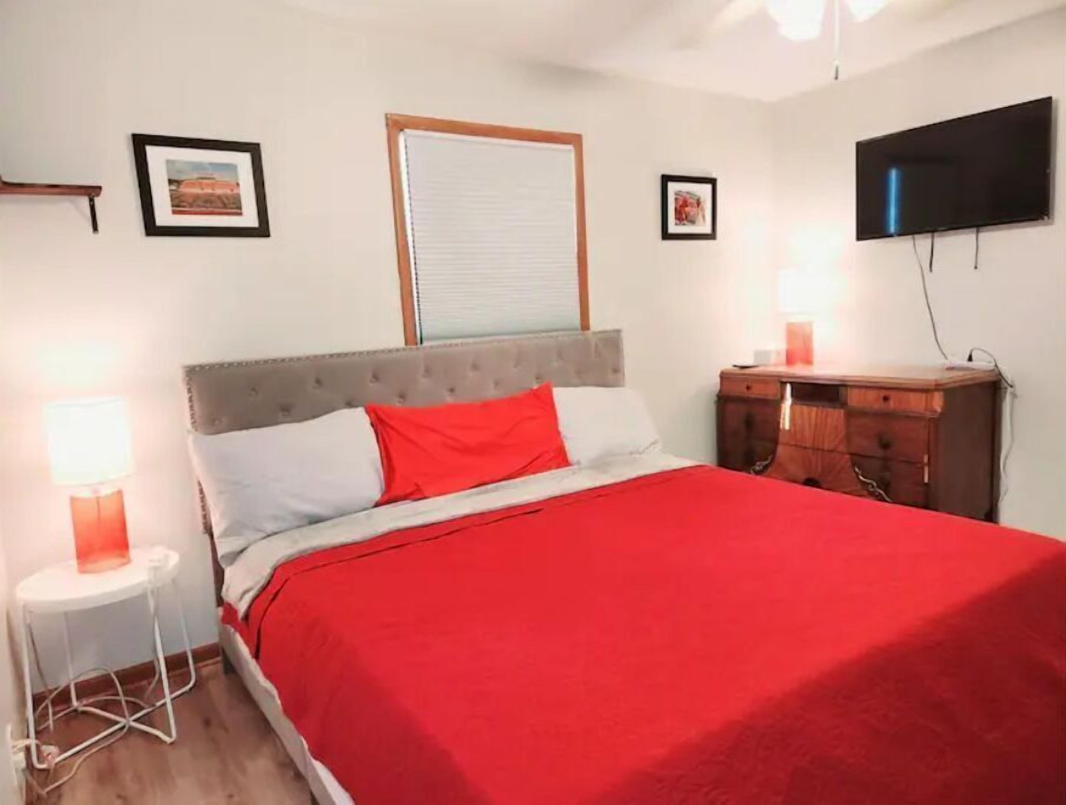 Une chambre à coucher avec un lit, une table de chevet, une commode, un téléviseur et des tableaux encadrés accrochés au mur.
