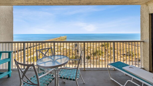 Een balkon met uitzicht op het strand en de oceaan, met een tafel en stoelen.