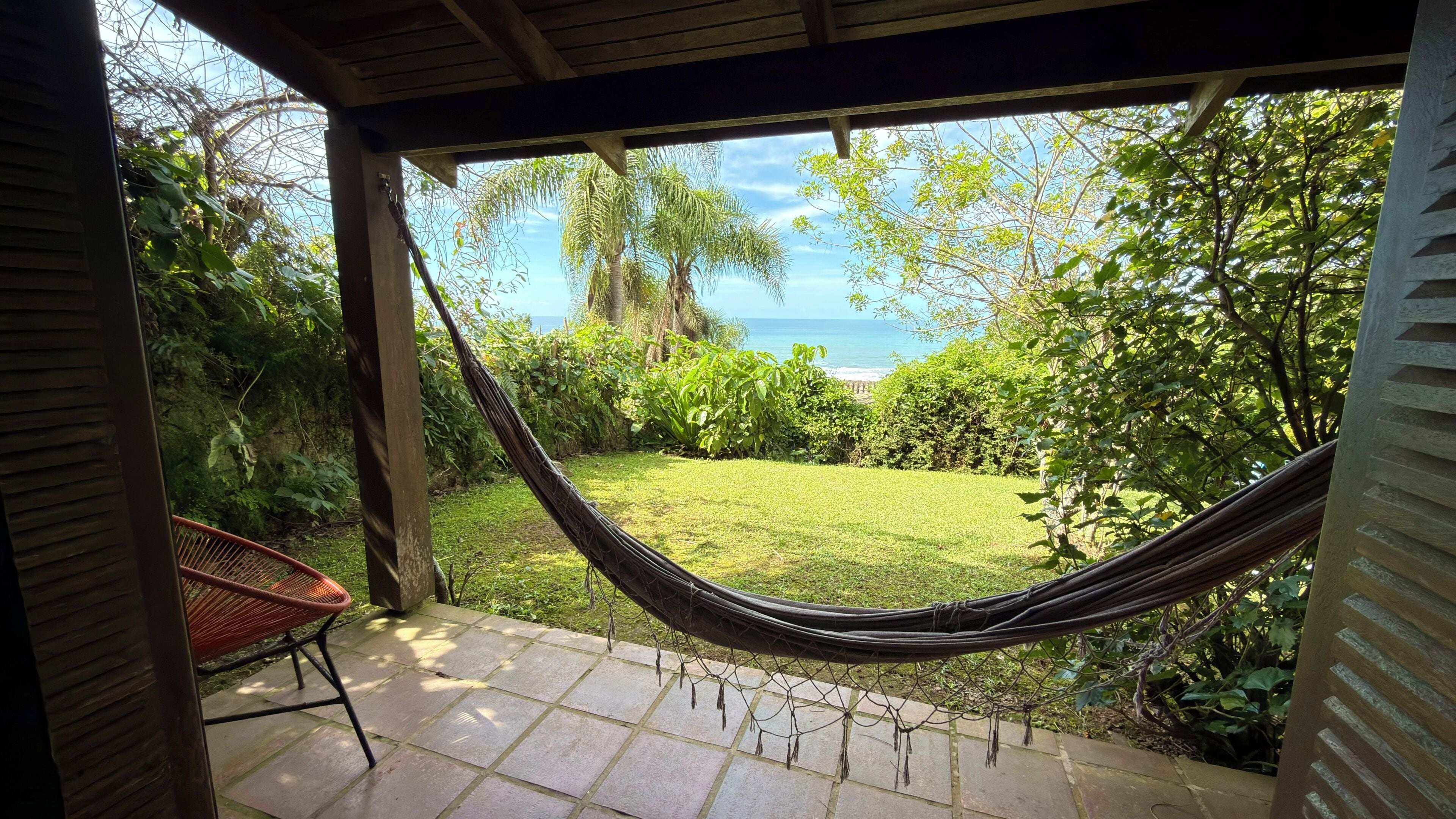 A hammock under a wooden pergola, a patio chair, and a view of the ocean.