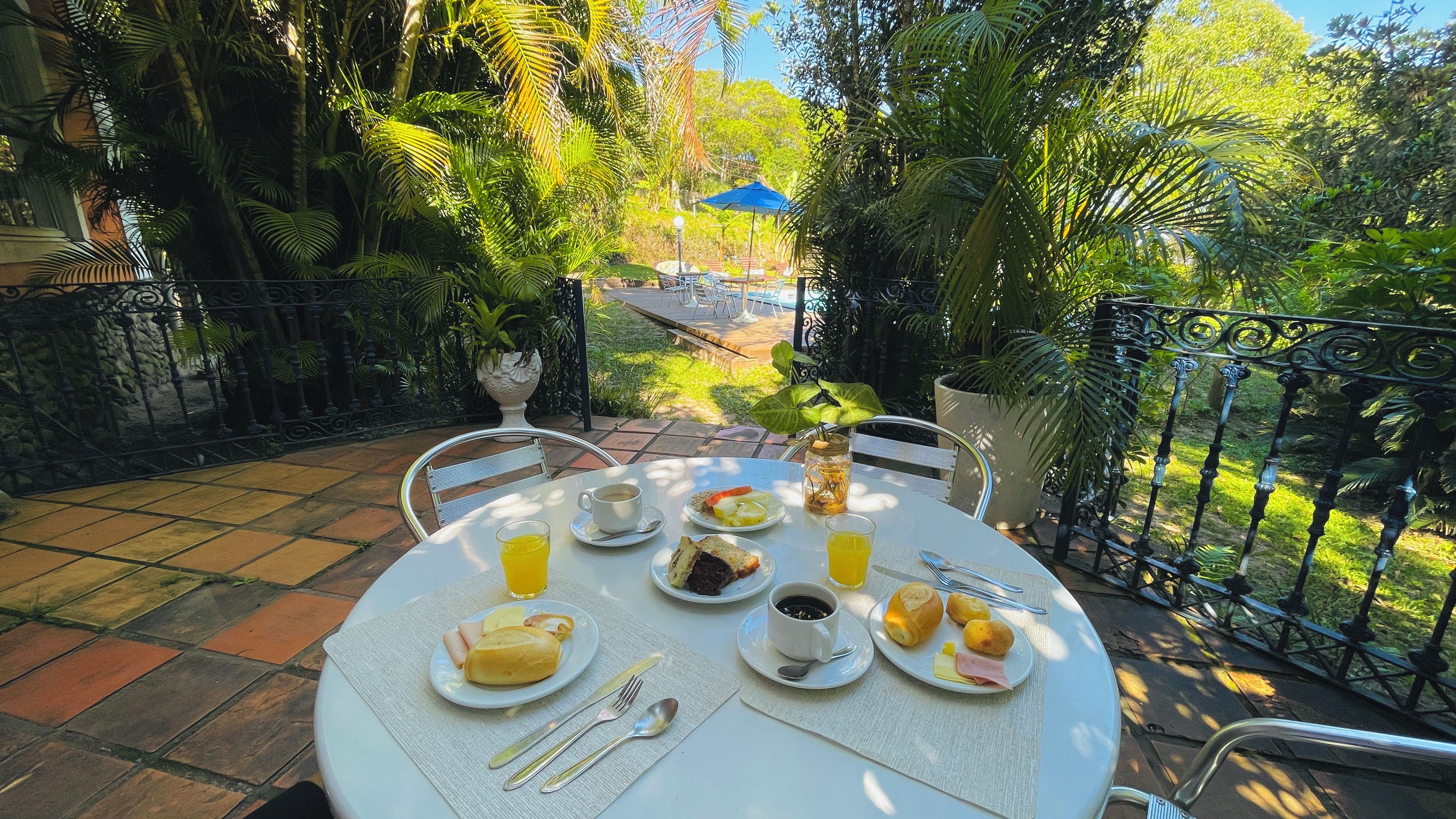 An outdoor dining table with breakfast items and a view of a garden.