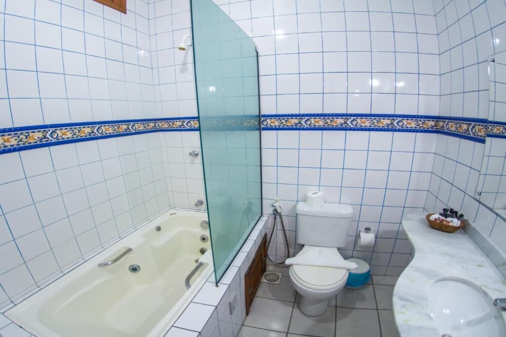 A bathroom with white tiled walls, a bathtub, a toilet, and a shower area.