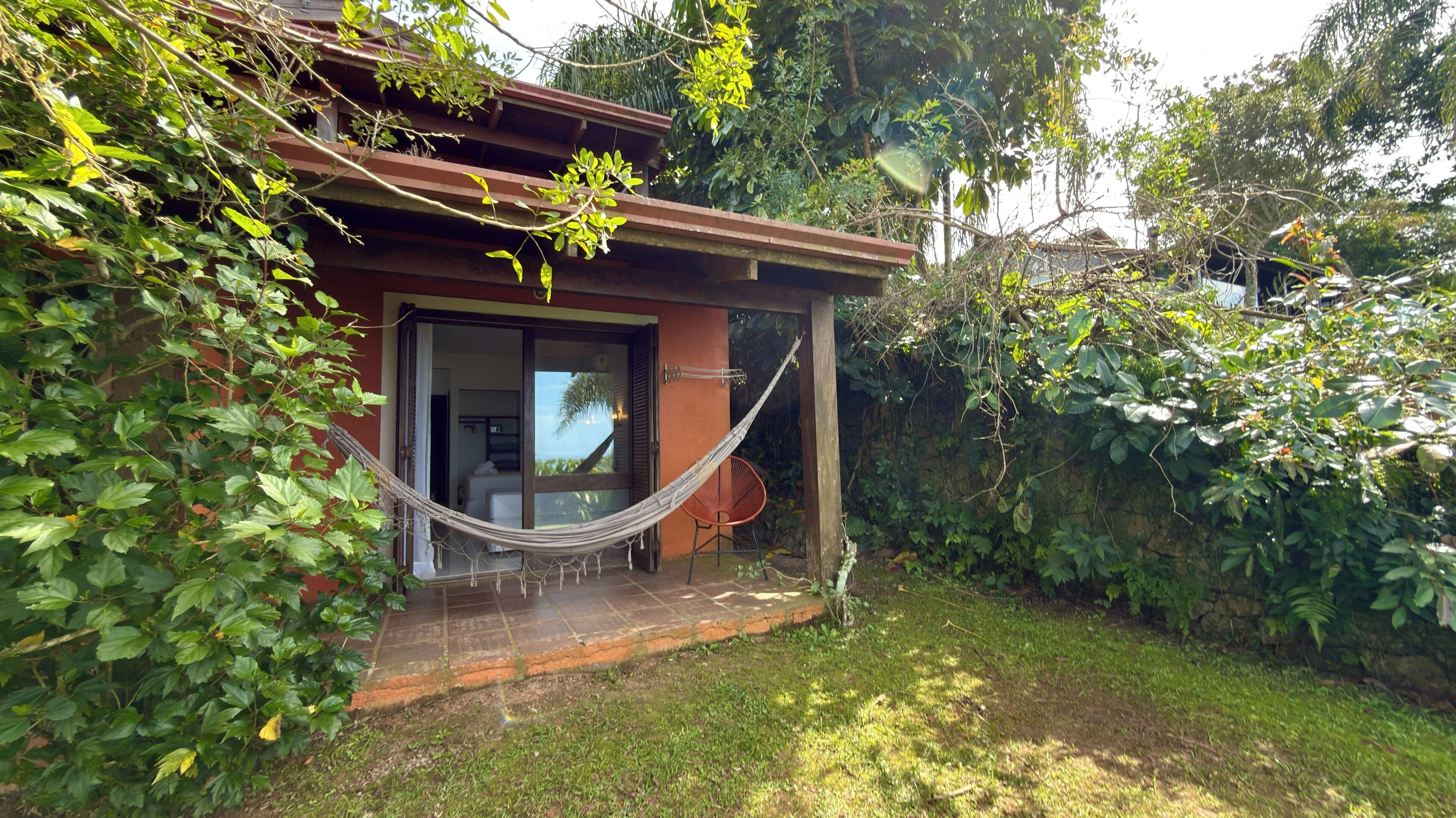 Una casa con una hamaca, una silla y una cama visible a través de la puerta abierta.