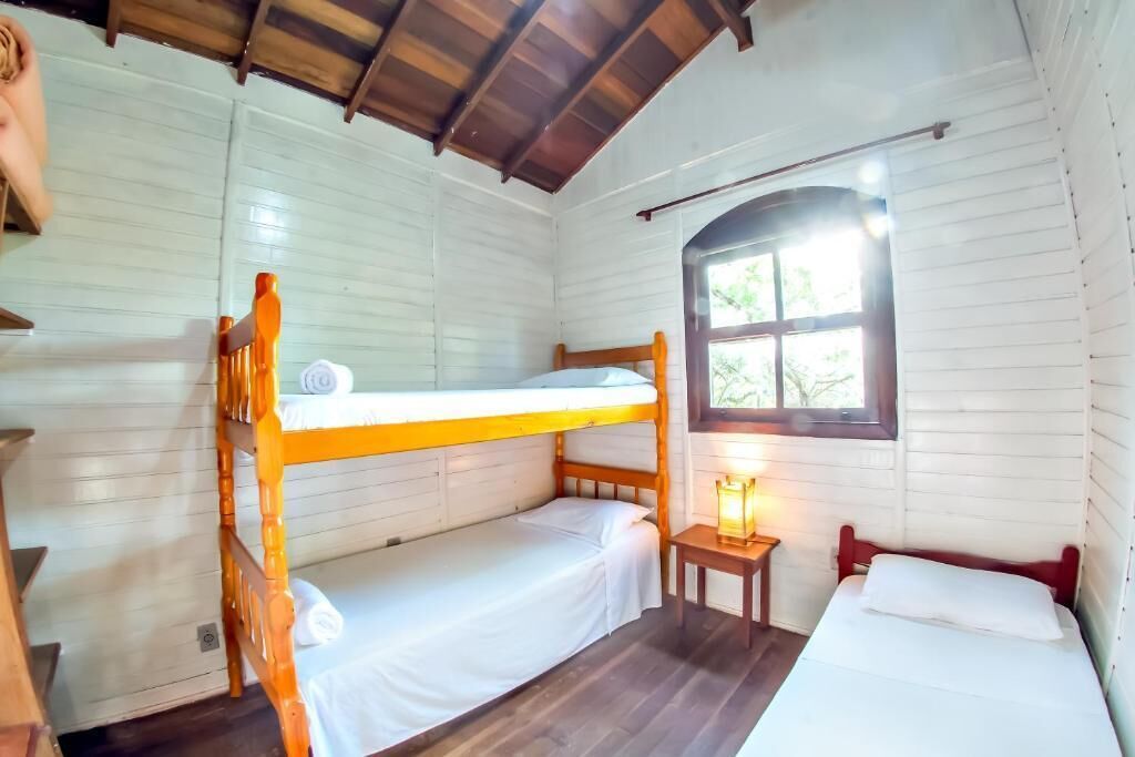 A room with bunk beds, a small table with a lamp, and a window with a view of greenery.