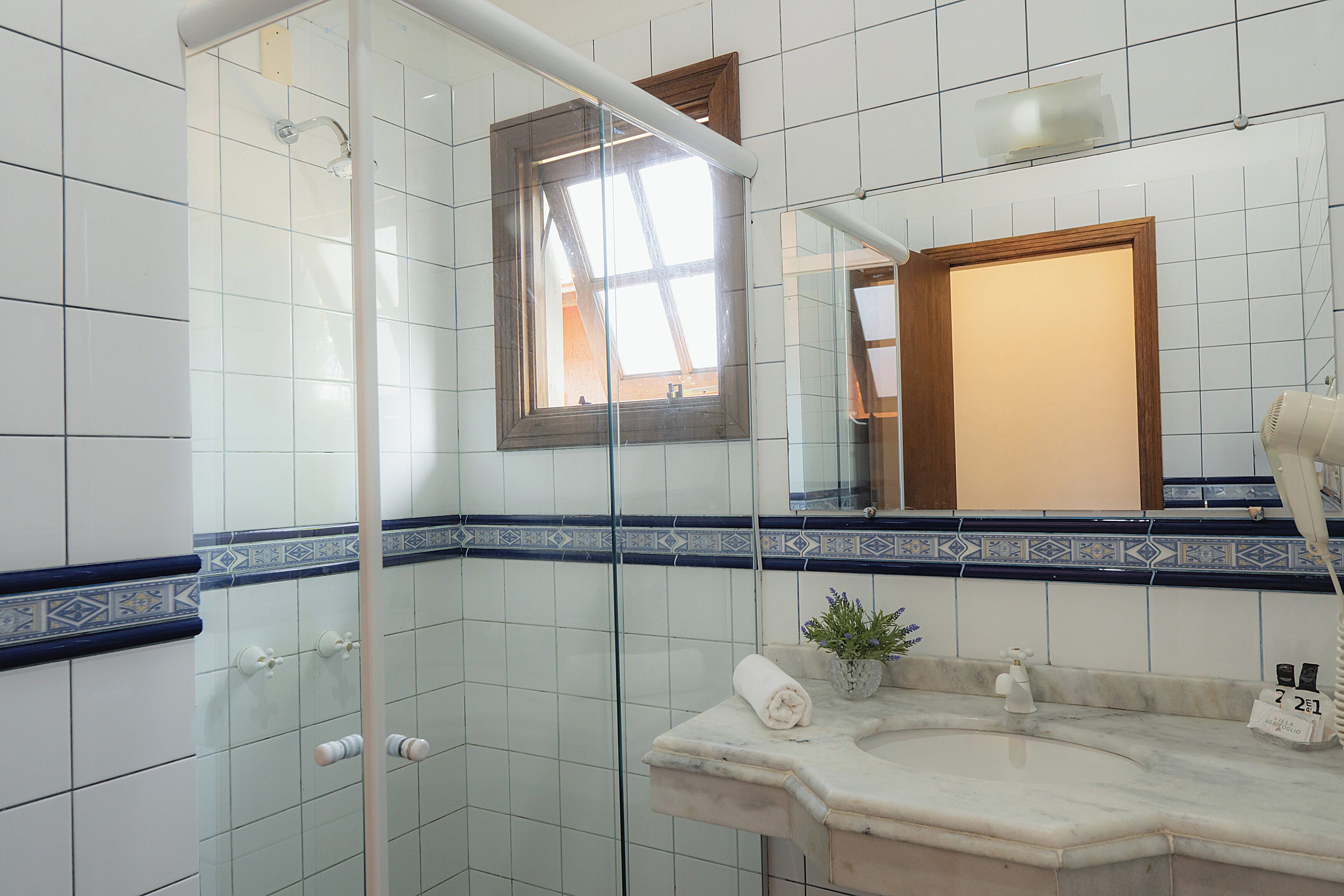 A bathroom with white tiles, a glass shower enclosure, a marble sink, and a small potted plant.