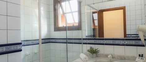 A bathroom with white tiles, a glass shower enclosure, a marble sink, and a small potted plant.