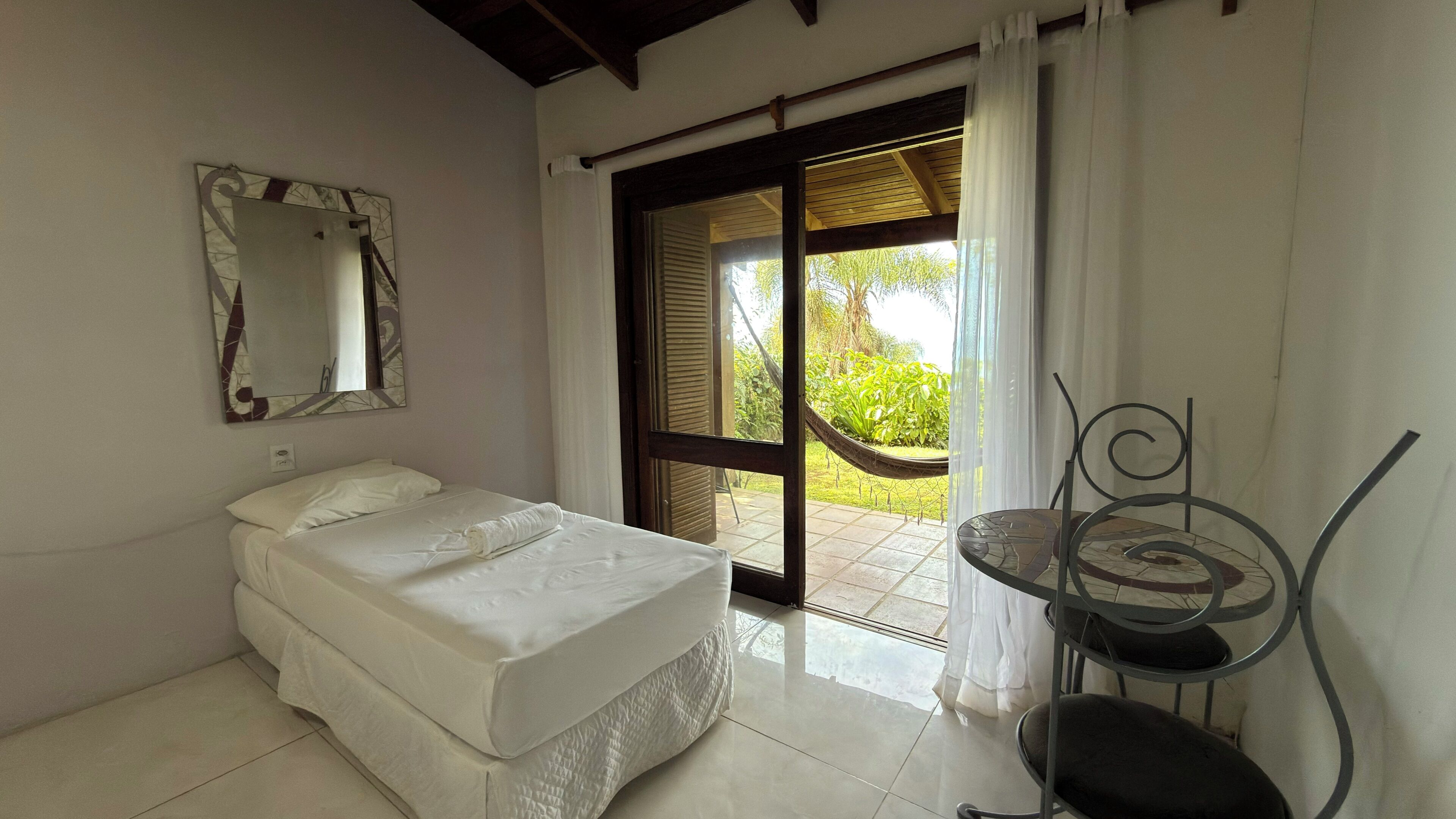 Un dormitorio con cama, una silla, una mesa, una ventana y una puerta que da a un espacio exterior.