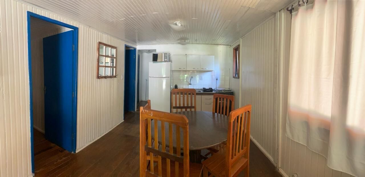 A dining area with a round table and four wooden chairs, a kitchen with white cabinets and a refrigerator, and a blue door leading to another room.