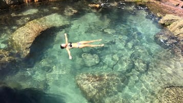 A person floating in a clear pool surrounded by rocky terrain.